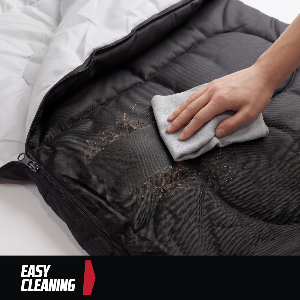 A hand wiping dirt off a black MoverX camping sleeping bag with a grey cloth.