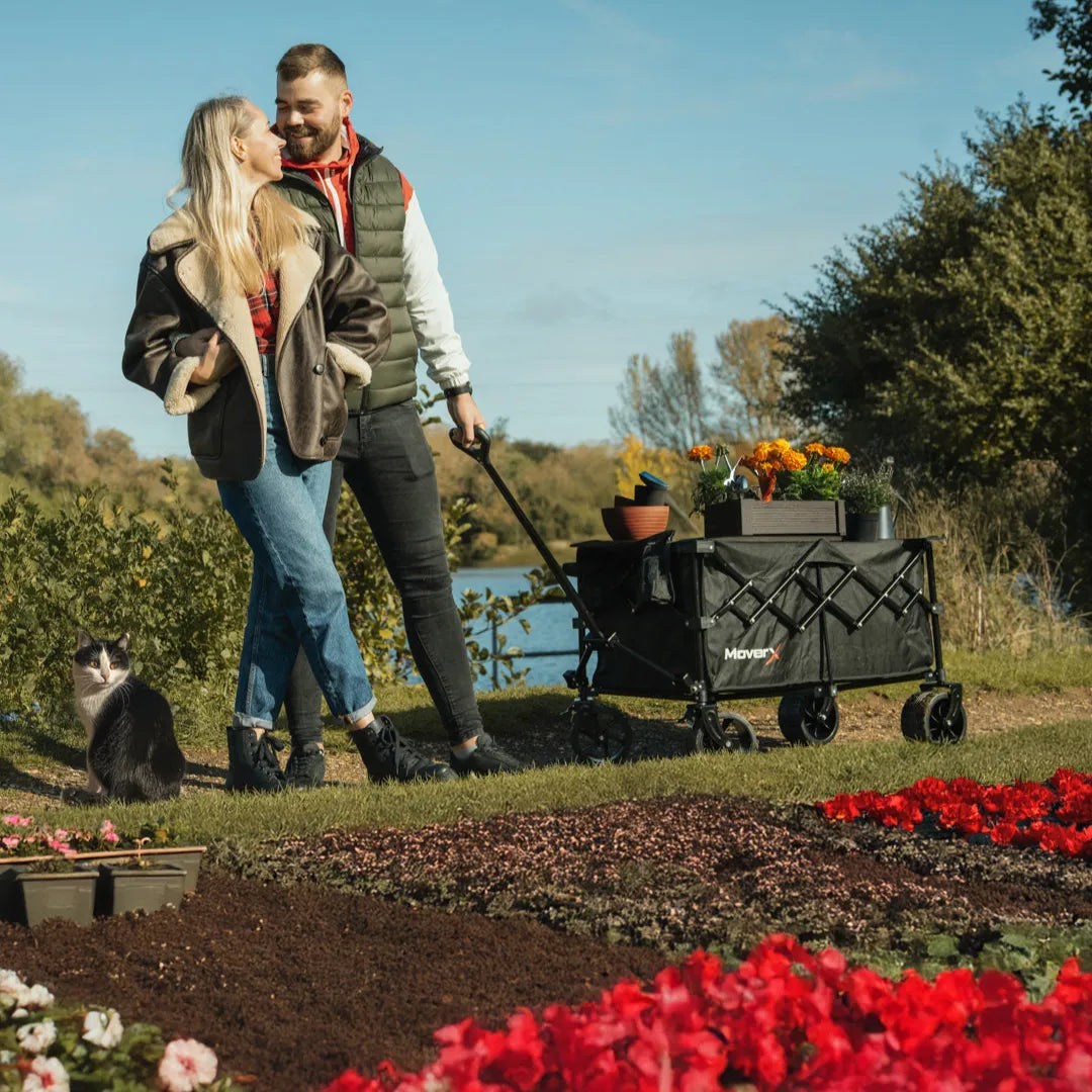 A couple using a MoverX foldable garden cart trolley to transport plants in a garden.