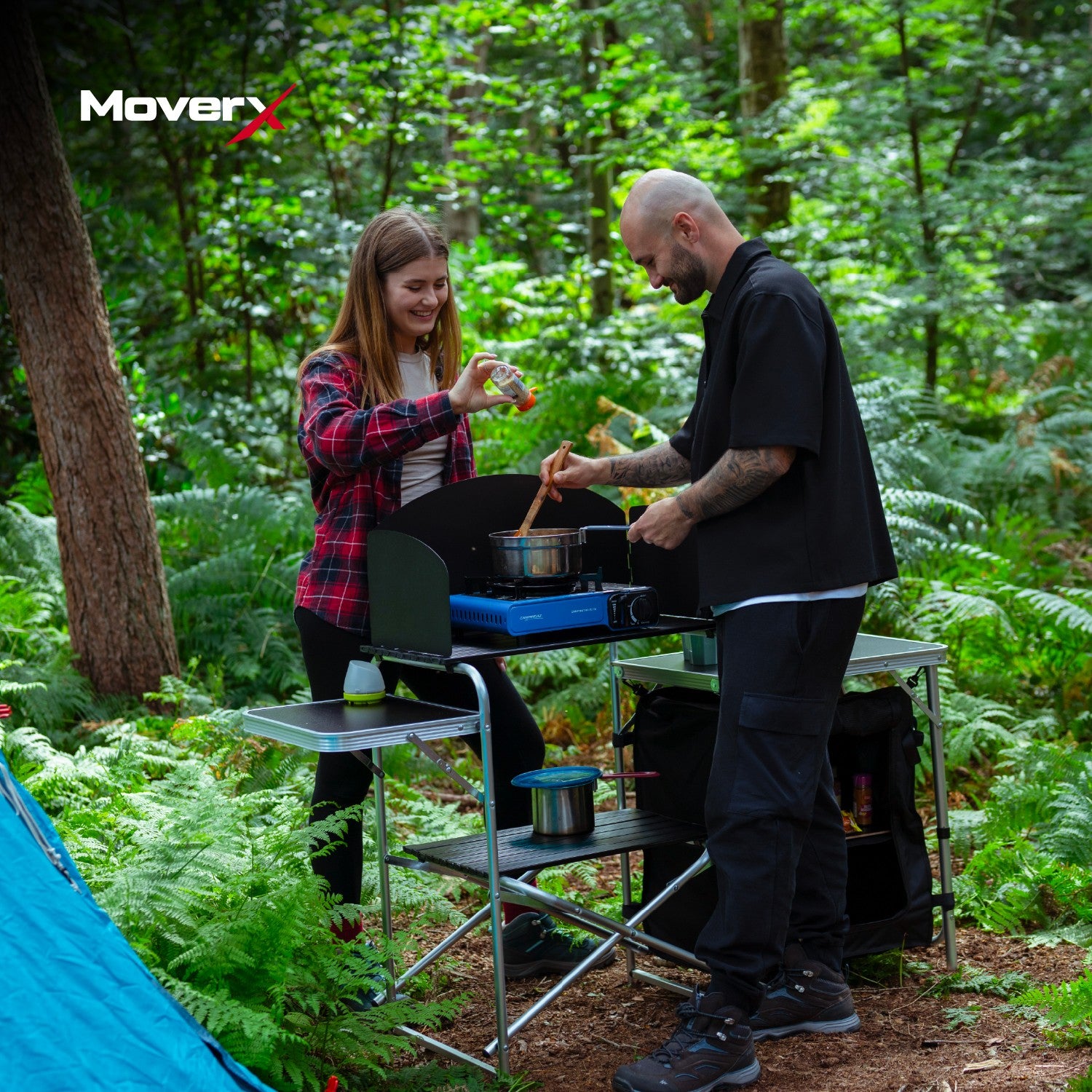 A man and woman cooking at a portable camping kitchen. 
